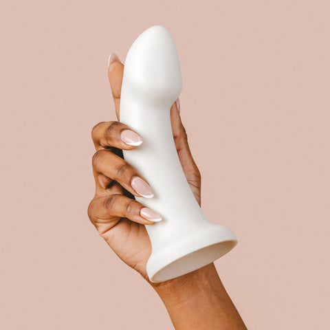 Hand holding The Natural Love Company Dill G-Curve, a silicone dildo with 6 inches of insertable length and girth of 5 inches at its thickest insertable point.