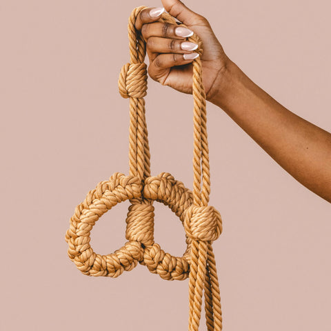 Hand holding The Natural Love Company Kanuka Handcuffs, soft handcuffs with control cord.