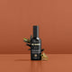 Styled bottle of face tan aqua mist with a sprig of olive leaf and sliced aloe vera against an orange background. 