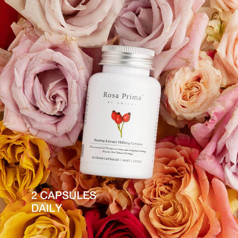 Unichi Rosa Prima Rosehip Extract 1500mg Complex 60 capsules lifestyle shot of the white bottle among pink, peach and yellow roses