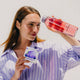 waterdrop Microdrink Boost Blackcurrant 12 servings lifestyle shot of a woman in a lilac striped shirt holding a glass of pink drink and the box