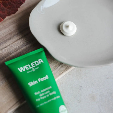 Weleda Skin Food tube on a wooden surface with a dollop of cream next to it.