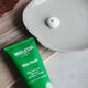 Weleda Skin Food tube on a wooden surface with a dollop of cream next to it.