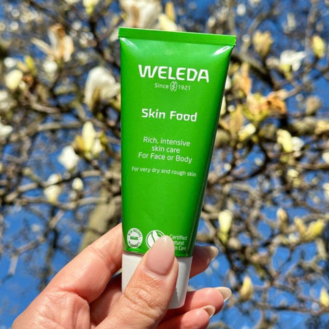 Weleda Skin Food tube held in a hand with a blurred natural background.