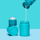 Turquoise roll-on applicator being refilled with sunscreen against a blue background. 