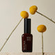 Wyuna Botanicals Golden Gem Face Cream 50ml lifestyle shot of the dark bottle among yellow billy button flowers on stems, styled lifestyle photo